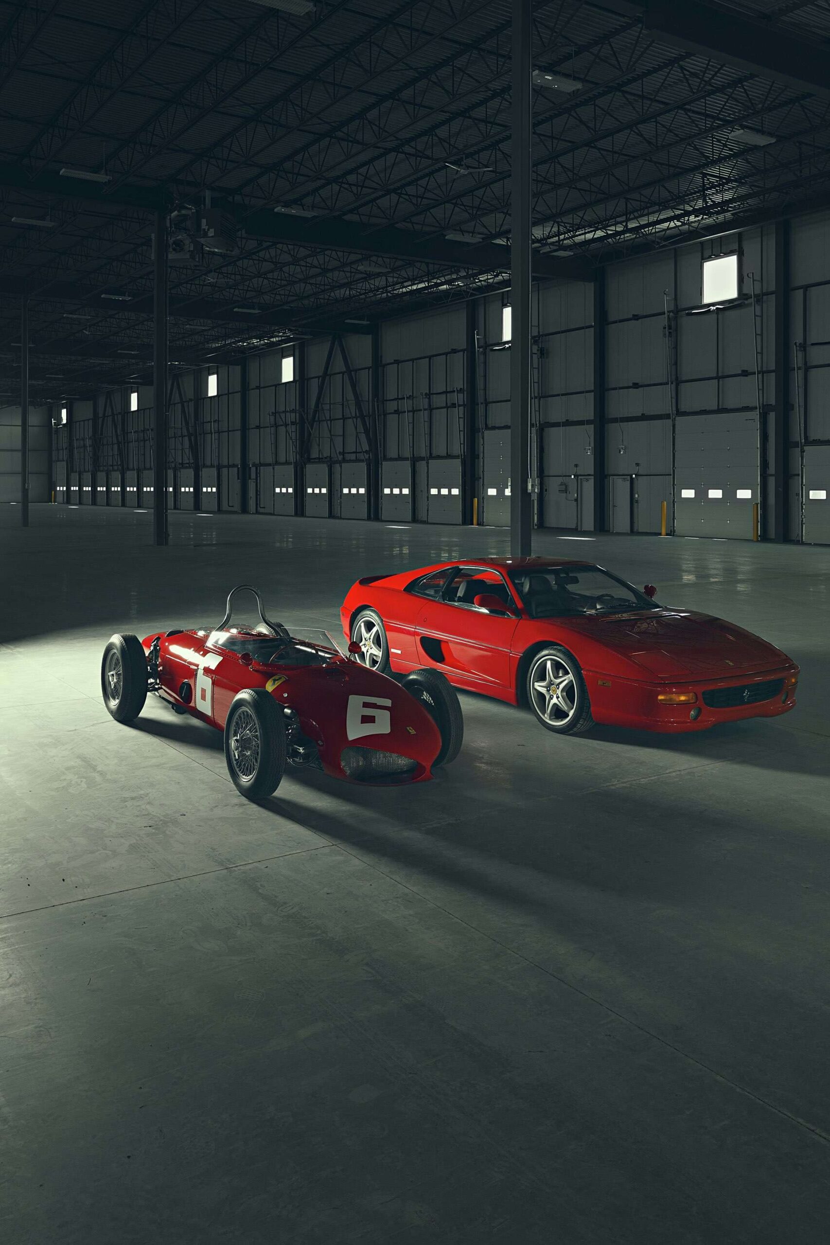 Two classic Ferrari super cars in a large warehouse under spotlight.