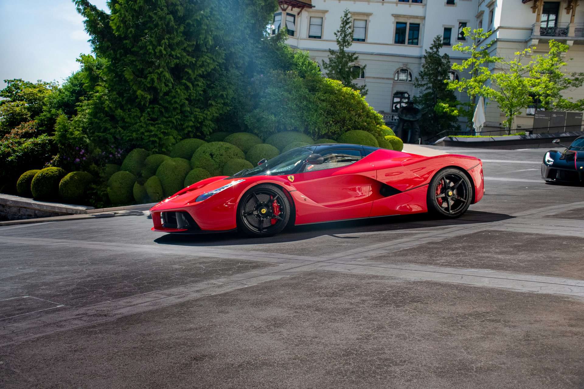 Side profile of a high performance Ferrari super car in front of a manor house setting.